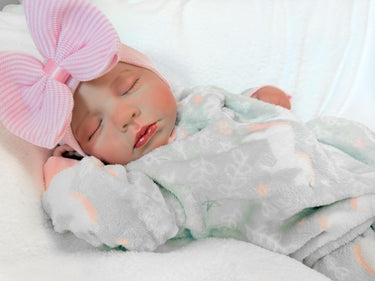 Newborn baby girl in a gray outfit with a pink bow, peacefully resting on a soft blanket.